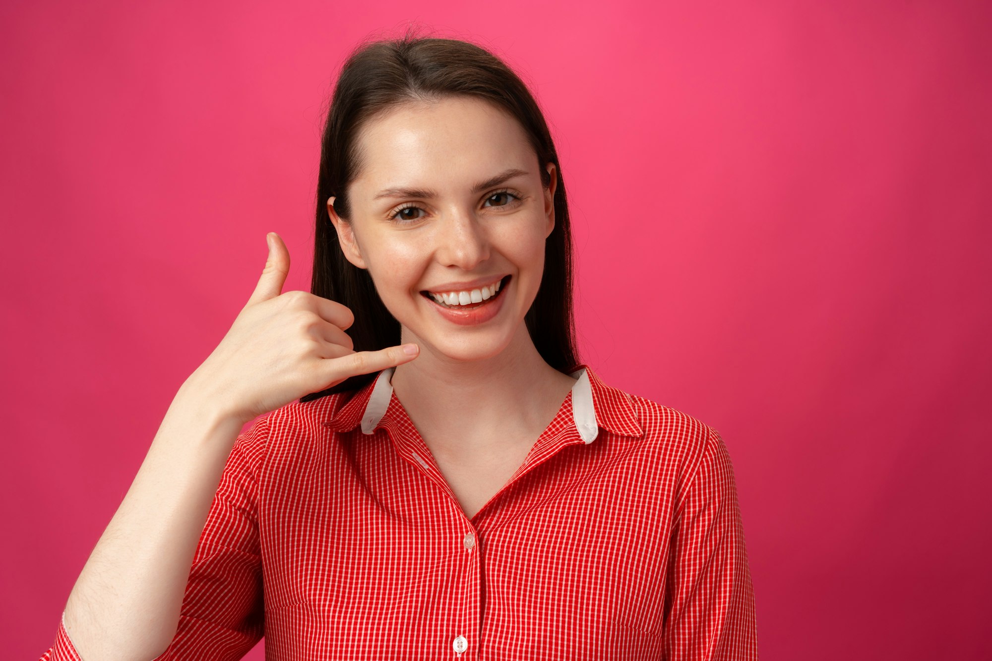 Young woman showing call me sign against pink background