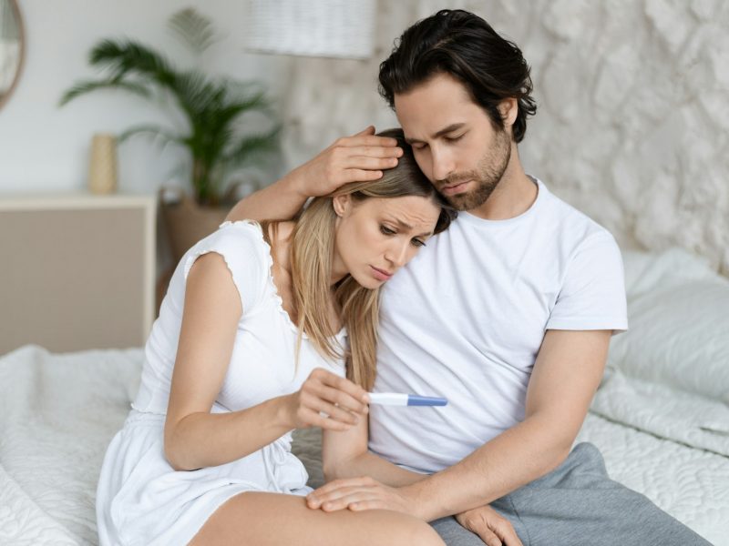 Infertility problem. Caucasian couple sitting on bed with negative pregnancy test result